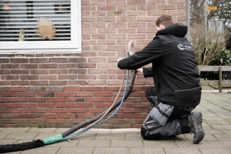 Medewerker van De Vries Isolatie voert spouwmuurisolatie uit aan de buitenkant van een woning