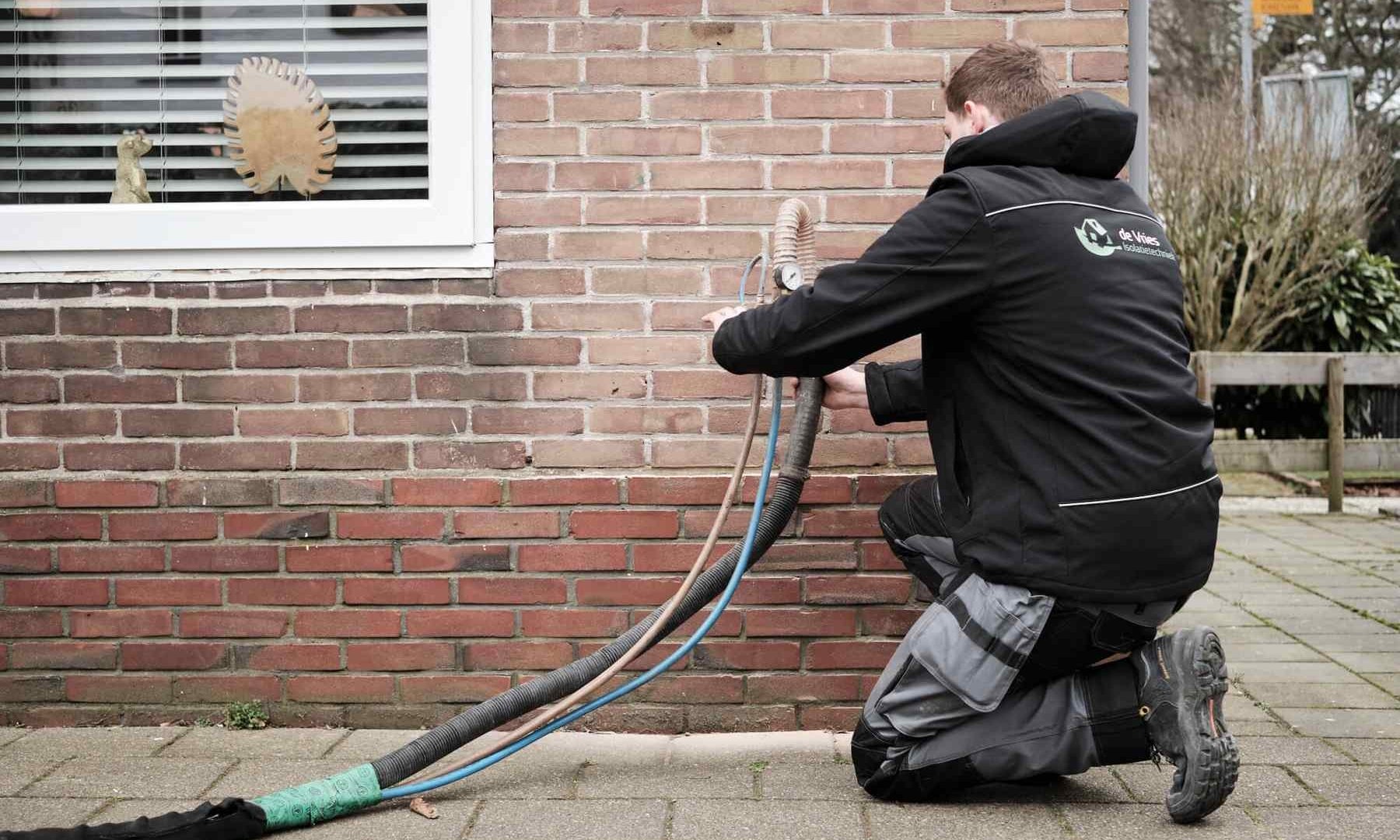 Medewerker van De Vries Isolatie voert spouwmuurisolatie uit aan de buitenkant van een woning